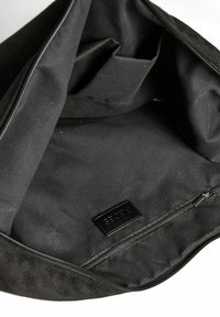 Crna platnena torba s mekom teksturom, s patentnim zatvaračem i unutarnjim džepom, ukrašena malom kožnom etiketom.