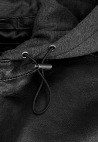 Svart lädertextil med grå textilhuva. Har en toggel och dragsko för justering. Slät yta, minimalistisk design.