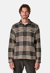 Camicia di flanella a quadri in grigio scuro, crema e bordeaux. Presenta una chiusura con bottoni frontale, colletto a punta e maniche lunghe con dettagli ai polsini.