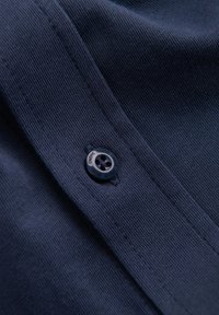 Marineblauwe textuurstof met een knop met vier gaten, gestikte naaddetail zichtbaar, gefocust op de knop en de stofweave.