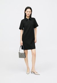 Vestido preto de manga curta com colarinho e fecho éclair frontal. Combinado com uma bolsa estampada e sapatos de salto fechado bege. Tecido de textura suave.