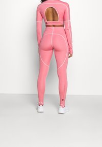 Rosa träningsset bestående av en långärmad topp med öppen rygg och högmidjade leggings. Slät textur med vita detaljer.