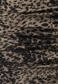 Gros plan sur un tissu beige avec un motif léopard noir irrégulier, montrant la texture et les plis visibles.