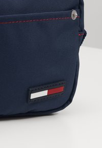 Námorně modrá látková taška s červeným stehem, cvokem a obdélníkovým logem se červenými, bílými a modrými pruhy.