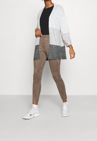 Cardigan grigio chiaro e grigio scuro realizzato in materiale morbido, abbinato a pantaloni in finta suede color beige e sneakers bianche. Design semplice e aperto.