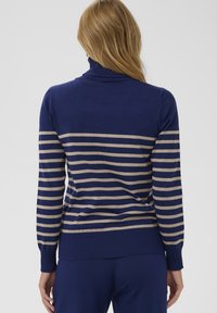 Navyblauer Rollkragenpullover mit horizontalen hellbeigen Streifen. Gerippte Bündchen und Saum, weiche Textur, figurbetontes Design und mittelgewichtiger Stoff.