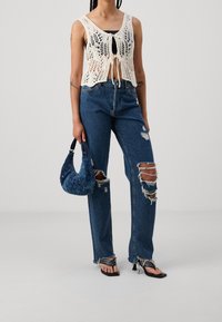 Szydełkowy krótki top z wiązaniem, niebieskie podarte dżinsy z postrzępionymi nogawkami oraz teksturowana niebieska torebka. Całość uzupełniają czarne sandały.