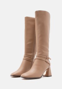 Botas altas de cuero beige con puntera cuadrada, doble correa y detalle de hebilla, cremallera lateral y tacones de bloque con acabado metálico.