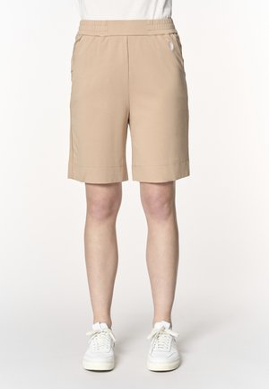 Pantaloncini beige fino al ginocchio con fascia elastica in vita e tasche laterali, indossati con sneakers bianche e top bianco.