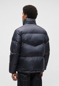 Casaco almofadado da Marinha com secções acolchoadas horizontais, colarinho alto e textura brilhante. Bolsos não visíveis na vista traseira.