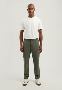 Witte T-shirt met ronde hals, olijfgroene cargobroek met zijzakken en witte sneakers. Eenvoudig ontwerp met een ontspannen pasvorm.