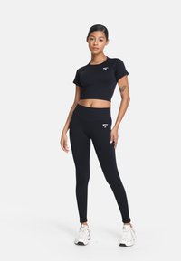 Czarny sportowy crop top i legginsy o wysokim stanie wykonane z elastycznego materiału, z małym białym logo na lewym piersiowym i nodze.