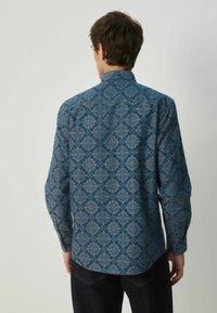 Dlhý rukáv košele z tmavozelenej tkaniny s zložitým svetlomodrým paisley vzorom. Obsahuje klasický golier a gombíkové manžety.