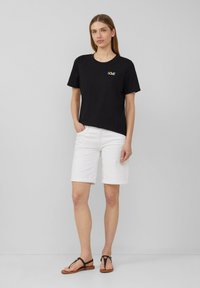 Zwarte katoenen t-shirt met "LOVE" geborduurd in regenboogkleuren, gecombineerd met witte denim shorts en bruine sandalen in een casual outfit.