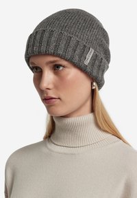 Szary, prążkowany beanie z podwiniętym mankietem i małą metką. Nosi się go z jasnobeżowym swetrem z golfem. Miękka faktura, dopasowany krój.