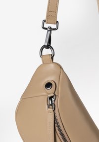 Borsa a mano in pelle beige con design curvo, dotata di zip e hardware neri. Include una tracolla rimovibile con clip in metallo.
