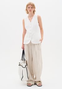 Vit ärmlös blus med v-ringning och knäppning, i kombination med ljusbeige vida byxor och en strukturerad tote-väska med svart kant.