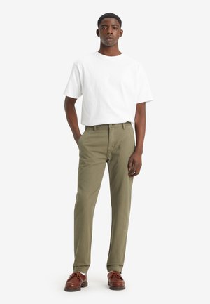 White cotton t-shirt paired with olive green cotton trousers, showcasing a straight leg design. Brown leather shoes complete the look.