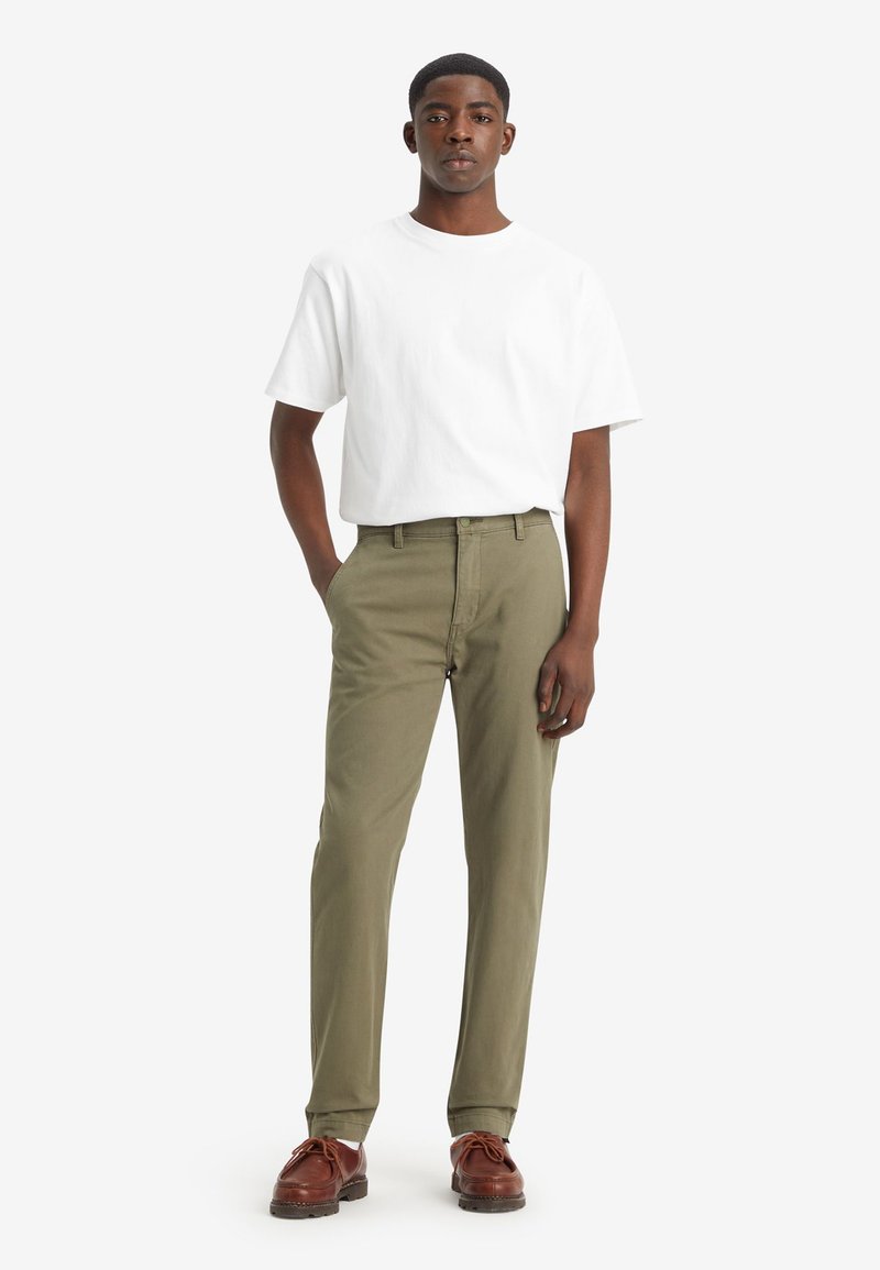 T-shirt bianco in cotone abbinato a pantaloni in cotone verde oliva, con un design a gamba dritta. Scarpe in pelle marrone completano il look.