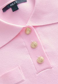 Roze gebreide poloshirt met een kraag, drie gouden knopen met reliëfdetail en een patchzak aan de linkerzijde.