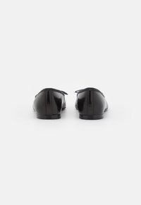 Ballerines en cuir noir avec une texture lisse, un bout arrondi et un design minimaliste. Présentent des coutures discrètes au niveau du talon et une fine bordure.