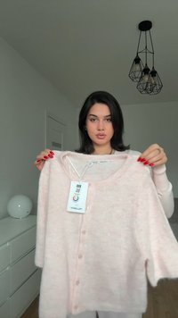 Cardigan scurt, roz deschis, cu mâneci scurte, dintr-un material moale, având un guler rotund, închidere cu nasturi și etichetă atașată. Design simplu, texturat.