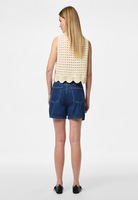 Kremasti kroštani kratki top s otvorenim uzorkom i valovitim rubom, uparen s tamnim trapericama koje imaju klasične džepove i opušteni kroj.