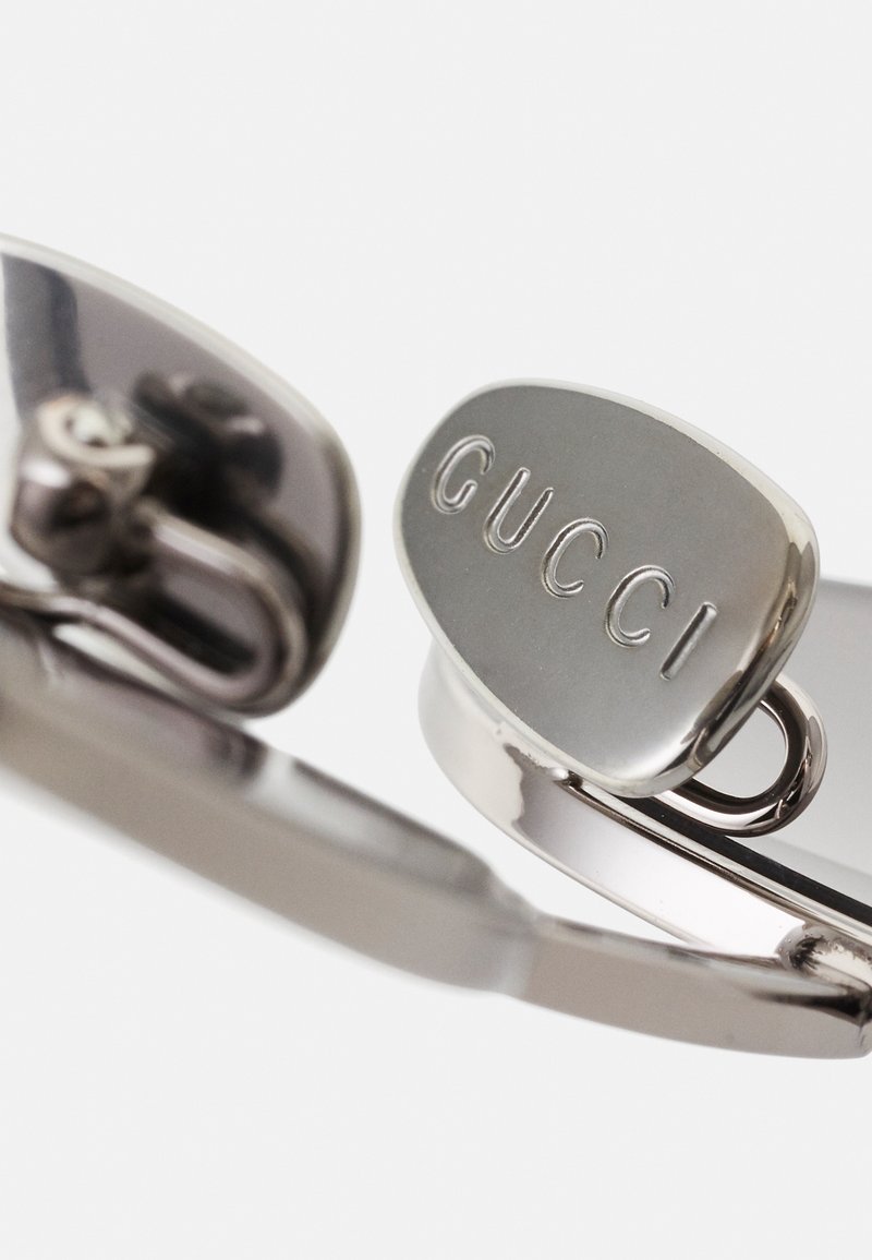 Ochelari de soare Gucci de nuanță argintie, având un emblemă ovală, cadru metalic și brațe curbate cu textură netedă și finisaj lustruit.