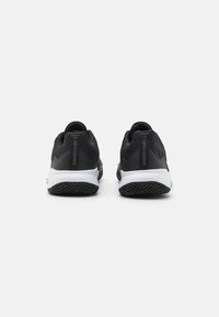 Ett par svarta sportskor med vita mellansålar och mönstrade svarta yttersålar, sedda bakifrån mot en neutral vit bakgrund.