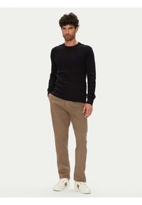 Schwarzer Pullover mit Zopfmuster und langen Ärmeln, kombiniert mit khakifarbenen Chinos und weißen Sneakern. Das Outfit zeichnet sich durch einen taillierten Schnitt und strukturierte Stoffe aus.