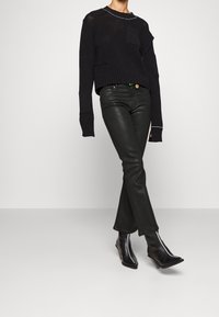 Suéter negro de punto con un diseño corto y tejido abierto. Combinado con pantalones vaqueros acampanados de cuero sintético negro y botas de cuña de punta fina.