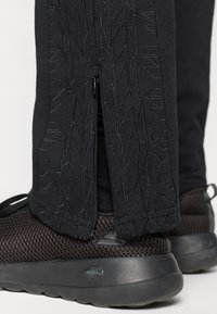 Zwarte sportbroek met ritszakken heeft een gestructureerd, reliëf profiel van autobanden. Gecombineerd met zwarte mesh sneakers.