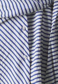 Tessuto a righe blu e bianche con un motivo testurizzato, caratterizzato da due chiusure a bottone. Le righe sono orizzontali e distanziate in modo uniforme.