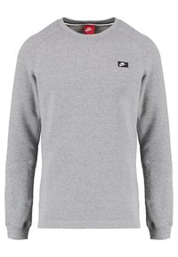 Harmaa pitkähihainen collegepaita, joka on valmistettu puuvillasekoitteesta. Siinä on pyöreä pääntie ja pieni musta Nike-logo rinnassa. Yksinkertainen muotoilu, jossa on resorit hihansuiden kohdalla.