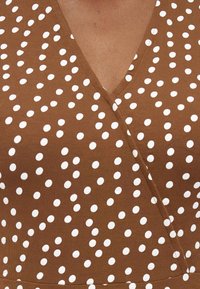 Καφέ φόρεμα τύπου wrap με λευκά πουά, που εμφανίζει λαιμόκοψη σε σχήμα V και υφή υφάσματος.