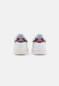 Bijele tenisice s bordo naglašenim petama, teksturirana gumena potplat, glatki sintetički gornji dio, s "new balance" logotipom na peti.