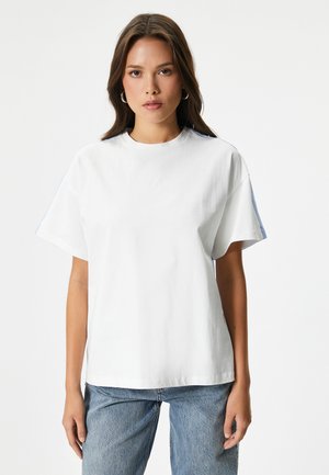 Witte katoenen t-shirt met korte mouwen, ronde hals en blauwe accenten op de mouwen. Eenvoudig ontwerp, zachte textuur en relaxte pasvorm.