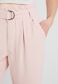 Rosa skräddarsydda byxor med bred midjeband, tygbälte, framveck och sidofickor. Slät textur och elegant design.