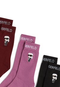 Calzini KARL LAGERFELD in bordò, rosa e nero. Ogni paio presenta un logo in stile cartone animato e il nome del brand ricamato in bianco sul risvolto.