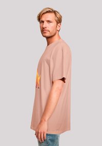 Light pink cotton t-shirt featuring short sleeves and a graphic of a dinosaur in yellow and orange. Straight cut with round neckline.