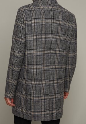 Karierter Mantel in Dunkelblau, Beige und Grau. Maßgeschneiderte Form mit einem strukturierten Kragen und langen Ärmeln. Der Stoff wirkt strukturiert und warm.
