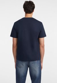 Marineblauwe t-shirt met korte mouwen van zacht katoen, met een klassieke ronde hals en een ontspannen pasvorm, gedragen met lichtblauwe denim jeans.
