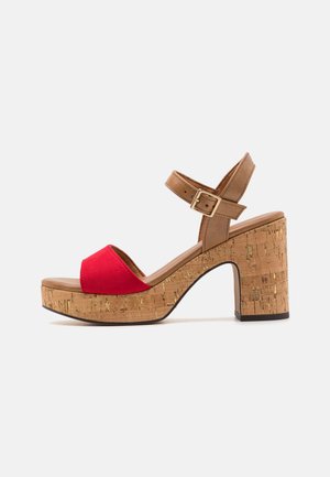 Sandalo aperto in suede rosso con una cinghia alla caviglia regolabile marrone, tacco in sughero e dettagli di superficie testurizzati, dotato di una base piattaforma.