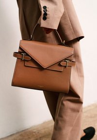 Borsa a tracolla in pelle marrone con una patta triangolare, dotata di finiture dorate e cuciture a contrasto. Manico per il trasporto incluso.