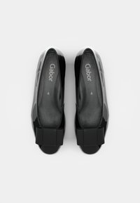 Scarpe slip-on nere con finitura lucida, dotate di ampi fiocchi in tessuto nero sulla parte anteriore e di una soletta testurizzata con logo stampato.