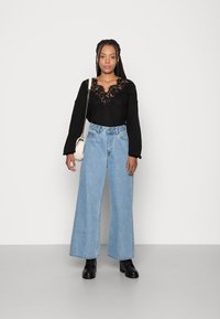 Sort strikket sweater med spidsekanter, parret med høj talje lyseblå vide jeans. Sorte ankelstøvler og en hvid skuldertaske fuldender looket.