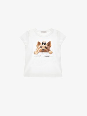 Camiseta blanca de manga corta con un estampado de un perro marrón que lleva un lazo negro y apoya las patas sobre un muro de ladrillos blancos.