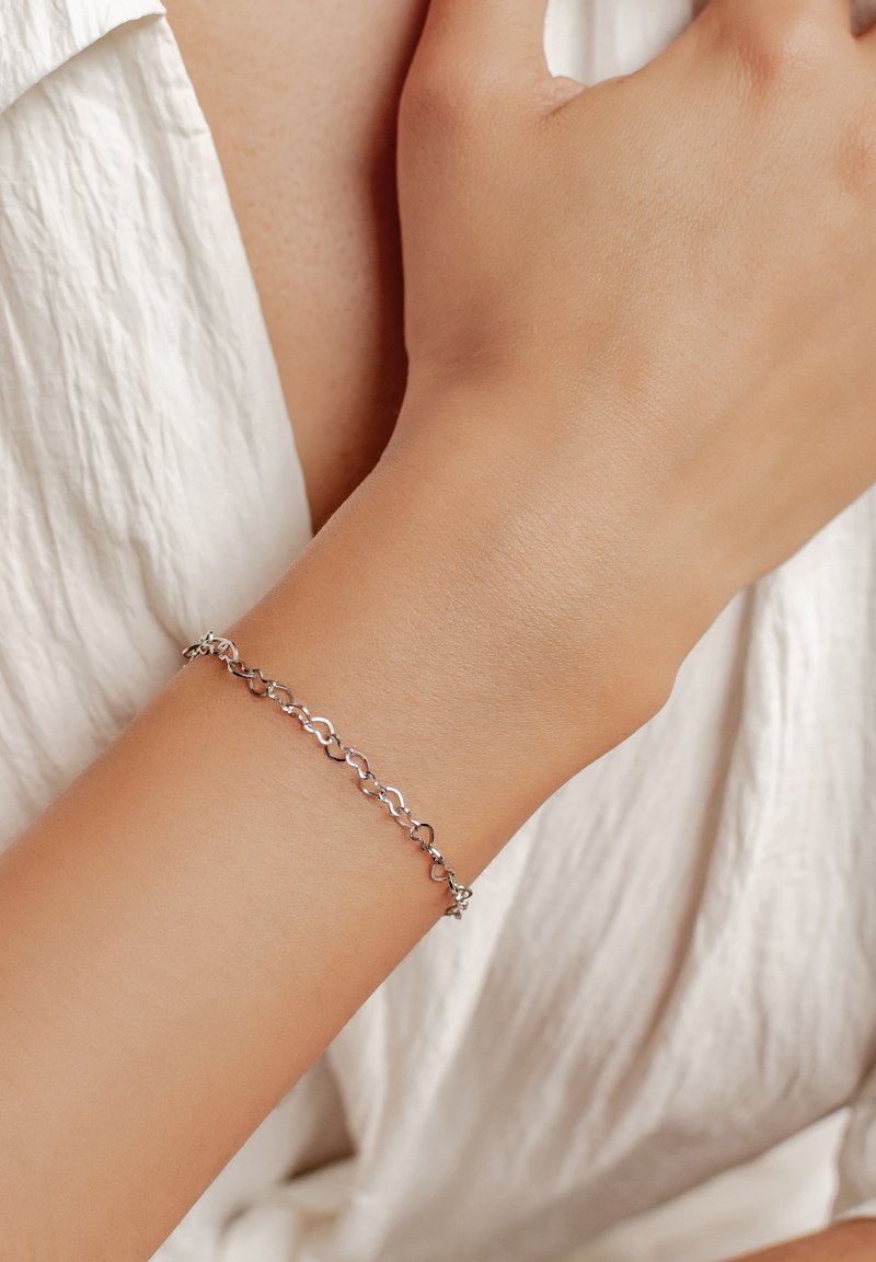 Silberne Kettenarmband mit länglichen, miteinander verbundenen Gliedern mit polierter Oberfläche; am Handgelenk vor einem hellen Stoffhintergrund getragen.
