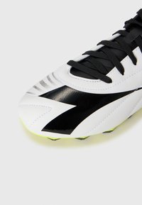 Close-up of a white soccer cleat with black laces and a bold black zigzag design on the toe area.