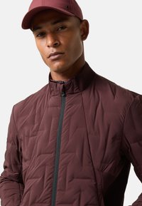 Bordeauxrote Steppjacke mit hohem Kragen und Reißverschluss vorne, mit strukturierten Einsätzen und atmungsaktiven Mesh-Akzenten.